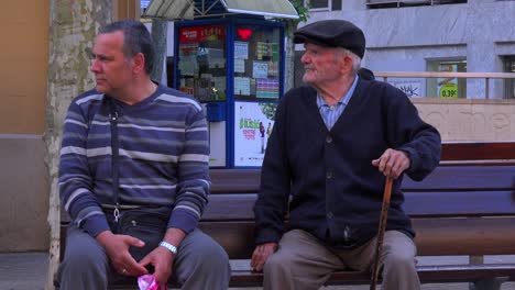 Two-men-sit-on-a-park-bench-in-Spain