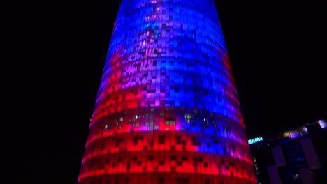 Tilt-up-remarkable-blue-and-red-skyscraper-at-night-in-Barcelona-Spain