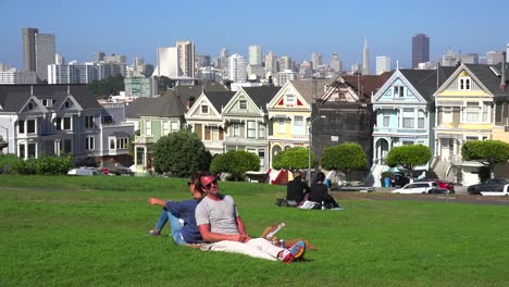 A-couple-sit-back-to-back-in-a-park-admiring-San-Francisco's-Victorian-houses