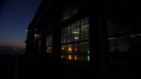Wide-shot-of-a-large-warehouse-or-factory-at-dusk-or-sunset-as-a-large-cargo-ship-passes-in-the-distance-3