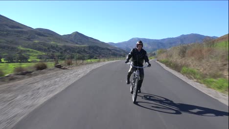 A-man-in-leather-jacket-drives-a-motorized-bicycle-along-a-country-road-1