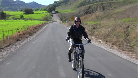 A-man-in-leather-jacket-drives-a-motorized-bicycle-along-a-country-road-2