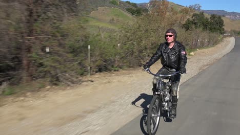 A-man-in-leather-jacket-drives-a-motorized-bicycle-along-a-country-road-3