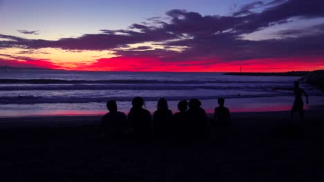 Kids-sit-in-silhouette-at-dusk-along-a-beach
