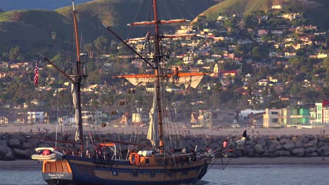 A-tall-clipper-ship-sails-at-sunset-with-the-city-of-Ventura-California-in-the-distance