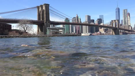 Water-level-establishing-shot-of-New-York-City-financial-district-with-Brooklyn-Bridge-foreground-and-boats-passing-under