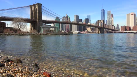 Water-level-establishing-shot-of-New-York-City-financial-district-with-Brooklyn-Bridge-foreground-and-boats-passing-under-1