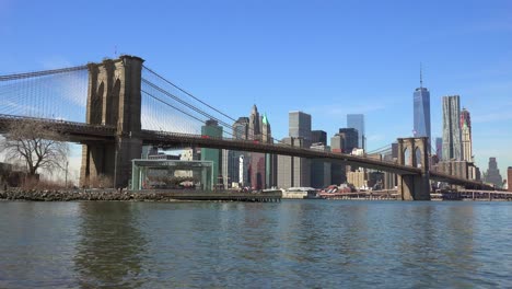 Water-level-establishing-shot-of-New-York-City-financial-district-with-Brooklyn-Bridge-foreground-and-boats-passing-under-2