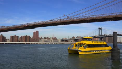 Un-Taxi-Acuático-De-La-Ciudad-De-Nueva-York-Se-Cruza-Frente-Al-Puente-De-Brooklyn.