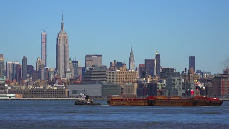 A-tugboat-pulls-a-barge-on-the-Hudson-River-in-New-York-City-with-the-Empire-State-Building-background