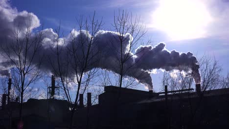 Global-warming-is-suggested-by-shots-of-a-steel-mill-belching-smoke-into-the-air-with-sun-background