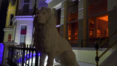 A-lion-statue-sits-in-front-of-an-elegant-row-of-houses-and-a-pub-in-a-British-town