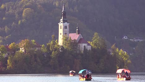 Ruderboote-Fahren-Bei-Sonnenuntergang-Zur-Insel-Auf-Dem-Bleder-See-Slowenien