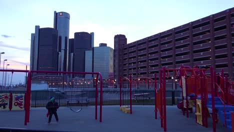 Der-GM-Turm-In-Der-Abenddämmerung-Entlang-Des-Detroit-River-In-Detroit-Michigan-Mit-Spielenden-Kindern-Im-Vordergrund