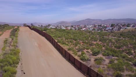 Slow-rising-aerial-along-the-US-Mexican-border-wall-fence-reveals-the-town-of-Tecate-Mexico