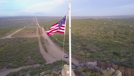 The-American-flag-flies-over-the-US-Mexico-border-wall-in-the-California-desert-as-a-border-patrol-vehicle-passes-below