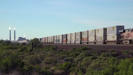 A-freight-train-heads-across-the-desert-with-an-industrial-site-background