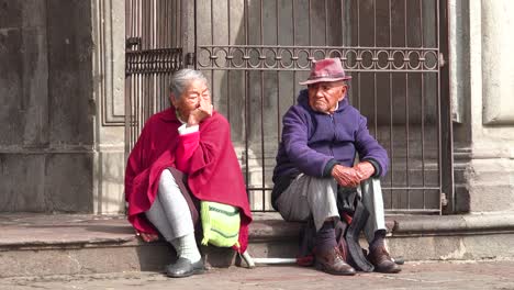 Ein-Altes-Paar-Sitzt-Auf-Der-Straße-Von-Quito-Ecuador-Und-Sieht-Den-Menschen-Zu