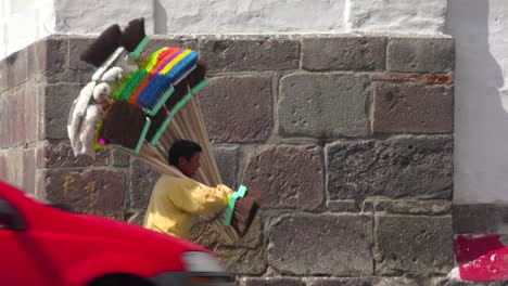A-man-carries-a-large-selections-of-brooms-down-a-street-in-Quito-Ecuador