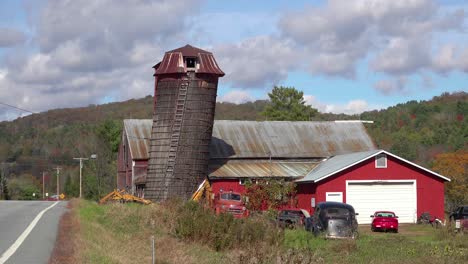 Old-cars-sit-outside-beside-a-red-barn-along-a-rural-road-in-Vermont