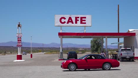 Toma-De-Establecimiento-De-Una-Gasolinera-Del-Desierto-Solitario-Y-Un-Hotel-Motel-Cafe-En-El-Desierto-De-Mojave-Con-Coche-Thunderbird-En-Primer-Plano