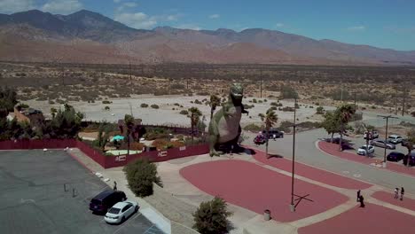 Aerial-over-a-giant-artifical-dinosaur-looming-over-visitors-as-a-roadside-attraction-in-the-Mojave-Desert-near-Cabazon-California
