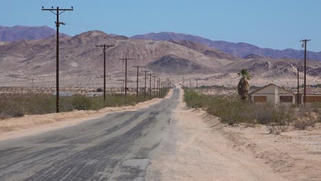Eine-Straße-Durch-Die-Mojave-Wüste-Mit-Verlassenen-Häusern-In-Der-Nähe