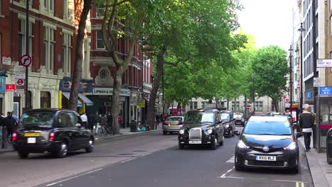 Traditionelle-Londoner-Taxis-Fahren-Eine-Straße-In-Einem-Viertel-Der-Innenstadt-Entlang