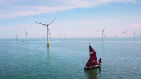 A-flat-bottomed-sailing-barge-sailboat-moves-up-the-Thames-River-Estuary-in-England-amidst-numerous-wind-turbine-windmills-3
