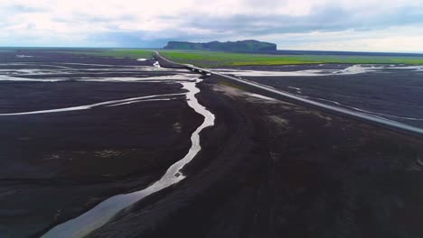 Aerial-of-a-car-driving-fast-along-a-road-and-bridge-over-a-large-dark-volcanic-flood-river-system-in-Iceland