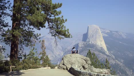 A-couple-takes-a-selfie-at-Washburn-Point-with-Half-Dome-and-High-Sierra-Mountain-Range-Yosemite-National-Park-CA