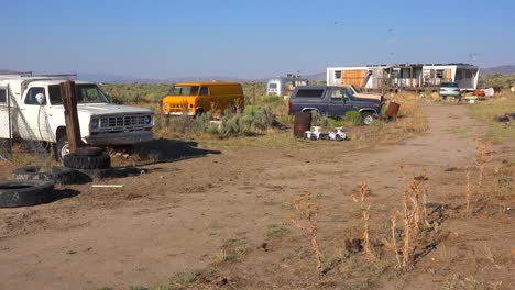 An-abandoned-mobile-home-in-the-desert-is-surrounded-by-old-trucks-and-cars-and-trash