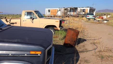 An-abandoned-mobile-home-in-the-desert-is-surrounded-by-old-trucks-and-cars-and-trash-3