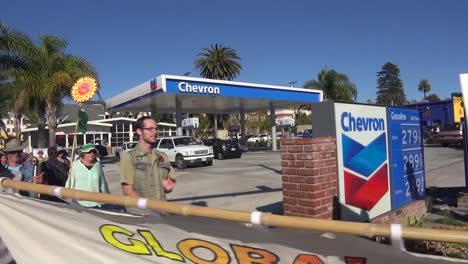 Global-warming-advocates-march-holding-signs-through-an-urban-area-and-past-a-gas-station