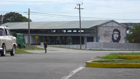 Un-Coche-Circula-Por-Una-Carretera-Cerca-De-Un-Edificio-Decorado-Con-Pintura-Revolucionaria-Che-En-La-Cuba-Comunista-1