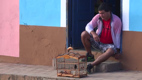 A-man-sits-on-the-street-with-his-pet-bird-in-a-cage-and-watches-the-world-go-by-Trinidad-Cuba