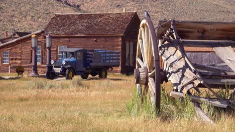 Old-green-pickup-truck-and-wagon-with-abandoned-house-background-in-the-ghost-town-of-Bodie-California