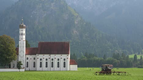 Gründungsaufnahme-Einer-Traditionellen-Deutschen-Bayerischen-Kirche-Mit-Einem-Traktor,-Der-Felder-Im-Vordergrund-Pflügt-1