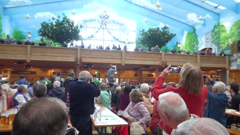 A-man-stands-on-a-table-and-downs-a-glass-of-beer-at-Oktoberfest-Germany