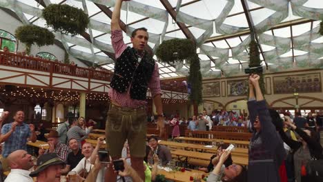 A-man-stands-on-a-table-and-downs-a-glass-of-beer-at-Oktoberfest-Germany-1