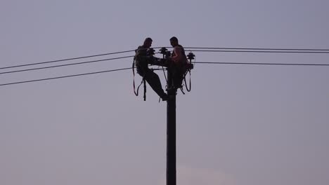 Two-men-in-silhouette-work-on-an-electrical-cable-atop-a-telephone-pole