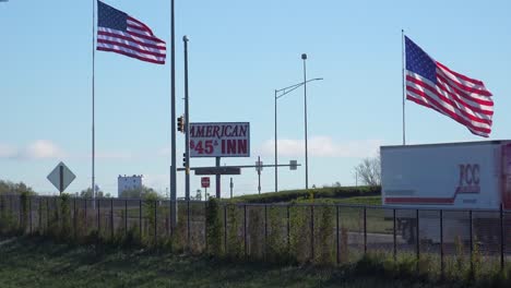 A-long-distance-trucker-passes-a-budget-hotel-and-american-flags-along-a-US-interstate-highway-in-America