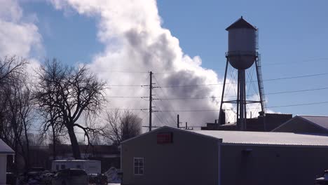 In-an-industrial-town-factory-smoke-pours-forth-from-behind-a-water-tower