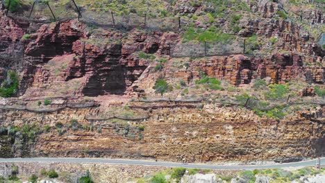 Una-Toma-Aérea-De-Un-Ciclista-Que-Viaja-Por-Una-Peligrosa-Y-Estrecha-Carretera-De-Montaña-A-Lo-Largo-Del-Océano-Chapmans-Peak-Road,-Cerca-De-Ciudad-Del-Cabo,-Sudáfrica