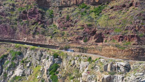 Eine-Luftaufnahme-Eines-Busses-Und-Autos,-Die-Auf-Einer-Gefährlichen-Schmalen-Bergstraße-Entlang-Der-Ocean-Chapmans-Peak-Road-In-Der-Nähe-Von-Kapstadt-Südafrika-Fahren