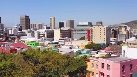 Aerial-over-treetops-reveals-colorful-Bo-kaap-Cape-Town-neighborhood-and-downtown-city-skyline