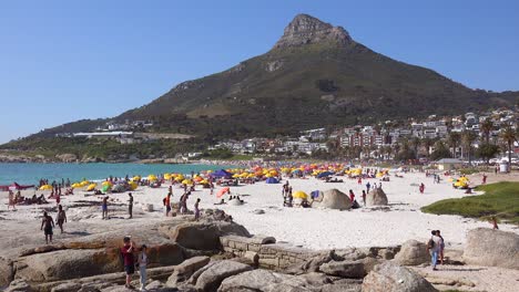 Establishing-shot-of-a-beautiful-busy-holiday-beach-scene-at-Camps-Bay-Cape-Town-South-Africa-with-Lions-Head-peak-background