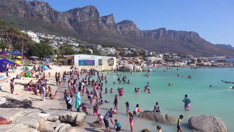 Eine-überfüllte-Und-Geschäftige-Urlaubsstrandszene-In-Camps-Bay-Kapstadt-Südafrika-Mit-Zwölf-Apostelbergen-Im-Hintergrund