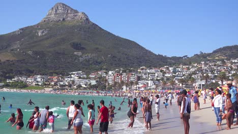 Eine-überfüllte-Und-Geschäftige-Urlaubsstrandszene-In-Camps-Bay-Kapstadt-Südafrika-Mit-Löwenkopfberg-Im-Hintergrund