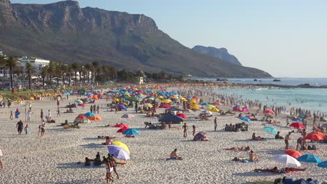Spectacular-aerial-over-a-crowded-and-busy-holiday-beach-at-Camps-Bay-Cape-Town-South-Africa-with-Twelve-Apostles-mountains-background